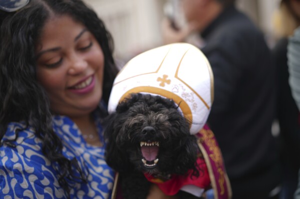 Meryl Espiniero from New York holds her dog Romeo Valentino at St. Peter's square where people wait to see smoke pour from the chimney of the Sistine Chapel where 133 cardinals are gathering on the second day of the conclave to elect a successor to late Pope Francis, at the Vatican, Thursday, May 8, 2025. (AP Photo/Andrew Medichini)