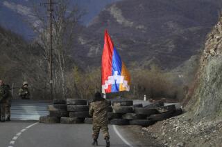 Un soldado de la etnia armenia camina con la bandera de Nagorno Karabaj el miércoles 25 de noviembre de 2020 en dirección a un retén cerca del poblado de Charektar. Éste se encuentra en la región separatista de Nagorno Karabaj, en una nueva frontera con el distrito Kalbajar entregado a Azerbaiyán. (AP Foto/Sergei Grits)