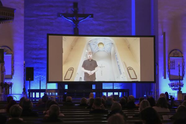 An AI-produced avatar of the Rev. Petja Kopperoinen, on the screen, addresses the attendees of St. Paul's Lutheran church in Helsinki, Finland, Tuesday, March 4, 2025.