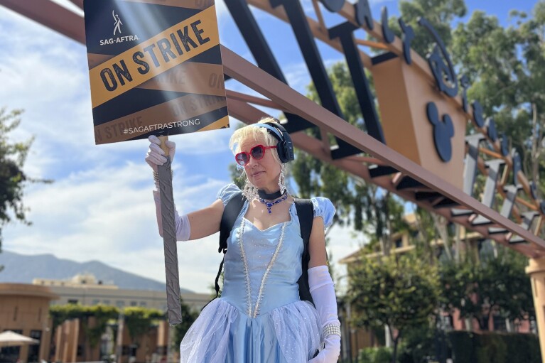 Andrea Calabrese, dressed as the character Cinderella, carries a sign on the picket line outside Walt Disney Studios on Wednesday, Sept. 27, 2023, in Burbank, Calif. Hollywood's writers strike was declared over Tuesday night when board members from their union approved a contract agreement with studios, bringing the industry at least partly back from a historic halt in production. The actors strike continues in their bid to get better pay and working conditions. (AP Photo/Rick Taber)