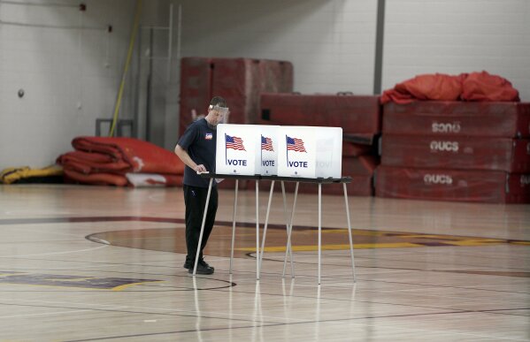 In this April 7, 2020, photo, Doug Milks disinfects voting booths after being used, as voters, ignoring a stay-at-home order over the coronavirus threat, cast ballots in the state's presidential primary election in the gym at East High School in Madison, Wis. The devastating coronavirus pandemic stands poised to reshape the political map this November. The virus has pummeled battleground states and alarmed Republicans who see early warning signs for an election that could be a referendum on President Donald Trump’s management of the crisis. (Steve Apps/Wisconsin State Journal via AP)