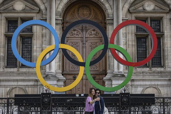 People take a photographs of the Olympic rings in front of the Paris City Hall, in Paris, Sunday, April 30, 2023. Olympic contestation is picking up online and starting to spill onto streets, because protesters are linking the Paris Games to unpopular pension reforms pushed through by French President Emmanuel Macron. (AP Photo/Aurelien Morissard)