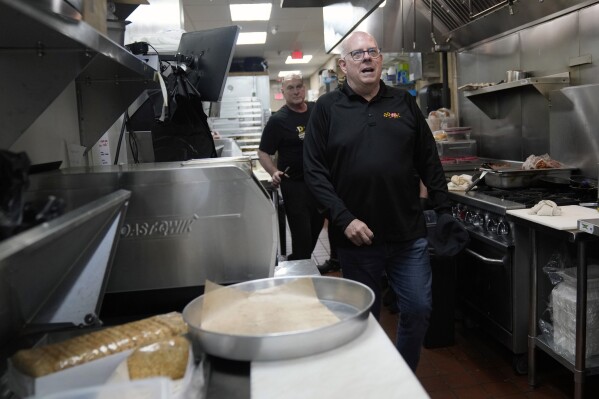 Former Maryland Gov. Larry Hogan, followed by Andy DePaola, walks through the kitchen of DePaola's Bagel and Brunch in Stevensville, Md., Friday, April 12, 2024, as he campaigns for the U.S. Senate. (AP Photo/Susan Walsh)