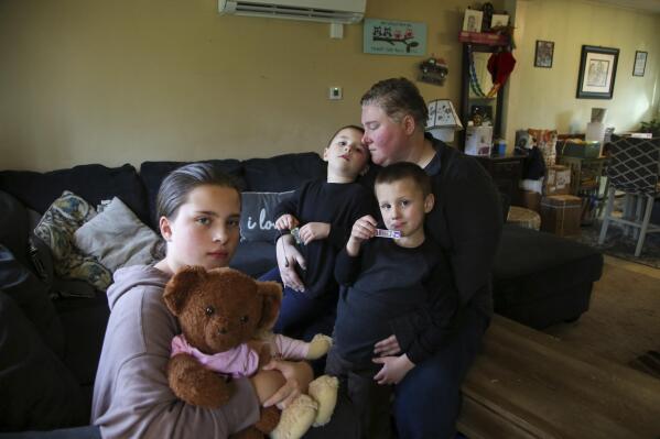 Jillian Philips sits with her children Macy, 10, and 4-year old twins, Emmett and Jude, right, in their home, Tuesday, May 2, 2023, in North Brookfield, Mass. Macy holds a teddy bear that houses a silver heart-shaped urn with some of the ashes of her deceased sister, Emilia, who died at 5 days old in 2015. Philips, who used the drug Mifepristone to manage her miscarriage, is concerned that other women who miscarry could suffer if the pill, also used for abortions, is taken off the market. (AP Photo/Reba Saldanha)