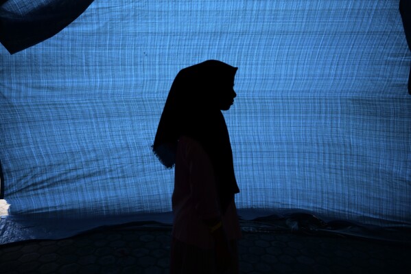 N, a 12-year-old ethnic Rohingya refugee identified by The Associated Press with only an initial, because she is a sexual assault survivor, stands in her tent at a temporary shelter in Meulaboh, Indonesia, on Thursday, April 4, 2024. N was among 75 people rescued from atop an overturned fishing boat off the Indonesian coast in March. Dozens of other Rohingya refugees died. (AP Photo/Reza Saifullah)