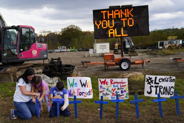 Bre Allard, accompanied by her children Lucy, 5, and Zeke, 8, plant crosses in honor of the victims of this week's mass shooting in Lewiston, Maine, Saturday, Oct. 28, 2023. The residents of Lewiston are embarking on a path to healing after a man suspected of killing several people earlier this week was found dead. (AP Photo/Matt Rourke)