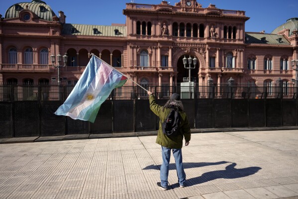 Santiago Farias, 62, waves an Argentine and Palestinian flag outside La Casa Rosada presidential office at the end of a march for job opportunities from San Cayetano church to downtown Buenos Aires, Argentina, Wednesday, Aug. 7, 2024, the feast day of St. Cajetan, known as the patron of the unemployed. (AP Photo/Rodrigo Abd)