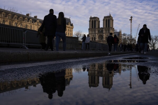 Pedestrians pass Notre Dame cathedral in Paris, Friday, Dec. 6, 2024. (AP Photo/Louise Delmotte)