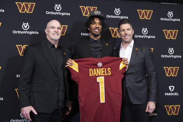 Washington Commanders' first round draft pick Jayden Daniels holds his Commanders jersey with head coach Dan Quinn, left, and general manager Adam Peters, right, following an NFL football news conference in Ashburn, Va., Friday, April 26, 2024. (AP Photo/Manuel Balce Ceneta)