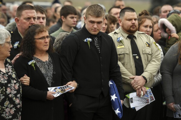 FILE - JD Prorok stands with his mom Renee Prorok for the three volley salute for Chief Deputy Ken Prorok on Thursday, Feb. 8, 2024, in Madison, S.D.. Moody County Chief Deputy Ken Prorok died in the line of duty during a vehicle chase. South Dakota prosecutors will seek the death penalty for a Sioux Falls man charged in Deputy Prorok's death who was struck while putting out spikes during a police chase. (Samatha Laurey/The Argus Leader via AP)