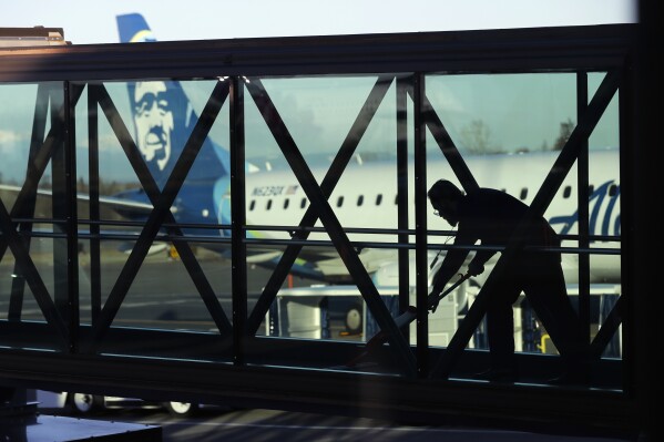 FILE - A worker cleans a jet bridge at Paine Field in Everett, Wash., before passengers board an Alaska Airlines flight on March 4, 2019. Seattle-based Alaska Airlines owns Horizon Air. An off-duty pilot riding in the extra seat in the cockpit of a Horizon Air passenger jet on Sunday, Oct. 22, 2023, tried to shut down the engines in mid-flight and had to be subdued by the crew, according to a pilot flying the plane. (AP Photo/Ted S. Warren, File)