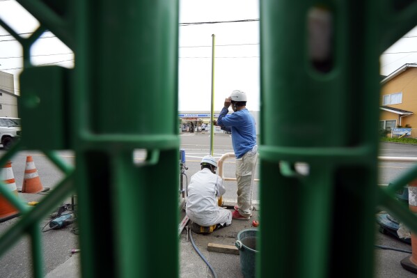 Workers set up a barricade near the Lawson convenience store, where the popular photo spot framing a picturesque view of Mount Fuji in the background Tuesday, April 30, 2024, at Fujikawaguchiko, Yamanashi Prefecture, central Japan. (AP Photo/Eugene Hoshiko)