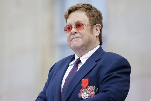 FILE - This June 21, 2019 file photo shows Elton John at a ceremony honoring him with the Legion of Honor in Paris. John is hosting a “living room” concert aimed at bolstering American spirits during the coronavirus crisis and saluting those countering it. The event was announced Wednesday by iHeartMedia and Fox. Alicia Keys, Billie Eilish, Mariah Carey, the Backstreet Boys, Tim McGraw and Billie Joe Armstrong are scheduled to take part in the concert airing at 9-10 p.m. Eastern Sunday on Fox TV and on iHeartMedia radio stations. (AP Photo/Lewis Joly, Pool, File)