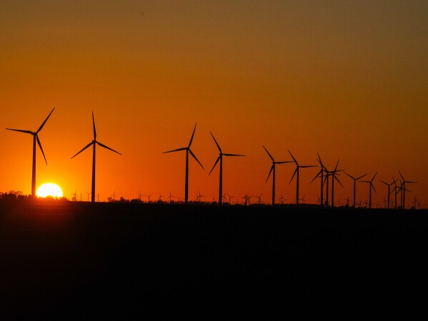 FILE - The sun sets behind wind turbines on a farm, Feb. 28, 2024, in Prairie Township, Ind. In campaigns for Congress and for governor around the country, candidates are talking about how green the grid should be (AP Photo/Kiichiro Sato, File)