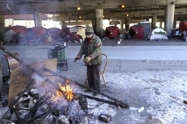 A man warms his hands by the fire he created across the street from a homeless encampment under a major interstate freeway Tuesday, Jan. 16, 2024, in Chicago. While the U.S. is shivering through bone-chilling cold, most of the rest of world is feeling unusually warm weather. Scientists Tuesday say that fits with what climate change is doing to Earth. (AP Photo/Charles Rex Arbogast)