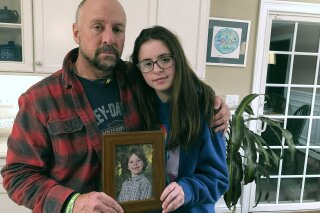 In this Dec. 3, 2019, photo, Mark Barden and his daughter Natalie Barden hold a photograph of Natalie's late brother, Daniel, at their home in Newtown, Conn. Daniel died in the Dec. 14, 2012, Sandy Hook Elementary School shooting that killed 20 first graders and six educators. Natalie, 17, is among Newtown students who have grown up to become young voices in the gun violence prevention movement. (AP Photo/Dave Collins)