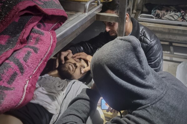 Two people mourn over the body of a man in a hospital morgue following Israeli airstrikes in Khan Younis, southern Gaza Strip, Tuesday, March 18, 2025. (AP Photo/Mohammad Jahjouh, File)