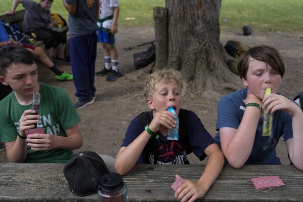 Campers eat popsicles while waiting at the zip line, Thursday, June 20, 2024, at YMCA Camp Kern in Oregonia, Ohio. As the first heat wave of the season ripples across the U.S., summer camps are working to keep their children cool while still letting the kids enjoy being outside with nature. (AP Photo/Joshua A. Bickel)