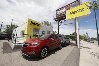 This May 23, 2020, photo shows rental vehicles parked outside a closed Hertz car rental office in south Denver. Rental car company Hertz plans to order up to 175,000 Chevrolet, Buick, GMC, Cadillac and BrightDrop electric vehicles from General Motors over the next five years. The deal includes electric vehicle deliveries through 2027 and will span a variety of vehicles such as SUVs, pickups and luxury automobiles. (AP Photo/David Zalubowski, file)