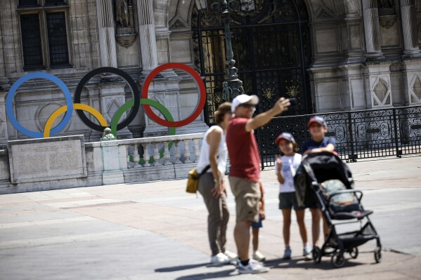 A family takes a selfie by the rings of the Olympic Games in front of the Paris townhall , Saturday, July 8, 2023 . The venue will host the start of the Olympic games' s marathon in the Paris 2024 Olympics. (AP Photo/Thomas Padilla)