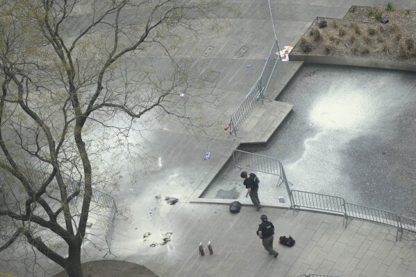 New York Police officers inspect a backpack left at the scene where a man lit himself on fire in a park outside Manhattan criminal court, Friday, April 19, 2024, in New York. Emergency crews rushed away a person on a stretcher after fire was extinguished outside the Manhattan courthouse where jury selection was taking place in former President Donald Trump's hush money criminal case. (AP Photo/Mary Altaffer)
