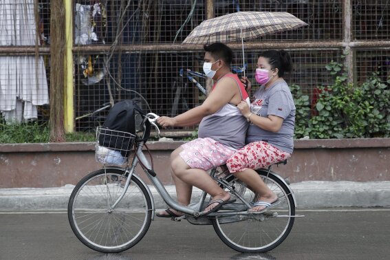 A couple uses an umbrella as they ride a bicycle through rain from Typhoon Vamco in Quezon city, Philippines on Wednesday, Nov. 11, 2020. Typhoon Vamco blew closer Wednesday to a northeastern Philippine region still struggling to recover from a powerful storm that left a trail of death and destruction just over a week ago, officials said, adding that thousands of villagers were being evacuated again to safety. (AP Photo/Aaron Favila)