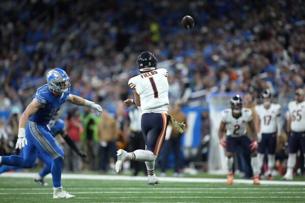 Chicago Bears quarterback Justin Fields (1) throws as Detroit Lions defensive end Aidan Hutchinson (97) gives chase during the second half of an NFL football game, Sunday, Nov. 19, 2023, in Detroit. (AP Photo/Paul Sancya)