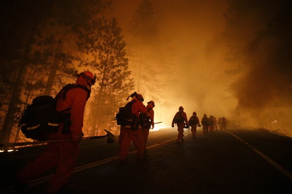 FILE - Inmate firefighters walk along Highway 120 after a burnout operation during the Rim Fire near Yosemite National Park, Calif., on Sunday, Aug. 25, 2013. California currently has about 1,250 prisoners trained to fight fires and has used them since the 1940s. It pays its "Angels in Orange" $2.90 to $5.12 a day, plus an extra $1 an hour when they work during emergencies. (AP Photo/Jae C. Hong, File)