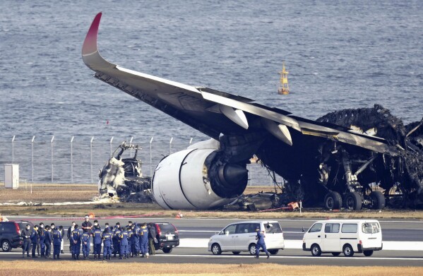 Police investigators gather beside the burn-out wreckage of Japan Airlines plane at Haneda airport on Thursday, Jan. 4, 2024, in Tokyo, Japan. A transcript of communication between traffic control and two aircraft that collided and burst into flames at Tokyo’s Haneda Airport showed that only the larger Japan Airlines passenger flight was given permission to use the runway where a coast guard plane was preparing for takeoff. (Kyodo News via AP)