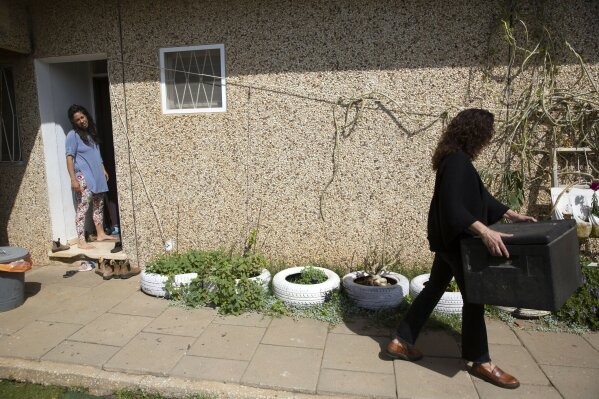 In this Monday, April 6, 2020 photo, emergency room doctor, Maayan Bacher, left, watches volunteer Einat Kedem leave after delivering a home-cooked meal, in the Israeli city of Raanana. More than 10,000 people have responded to Israeli Adi Karmon Scope’s Facebook plea to help overworked health-care professionals on the frontline of the country’s battle against the coronavirus pandemic. An army of volunteers is doing their grocery shopping, delivering home-cooked meals, babysitting for children and even walking pets. (AP Photo/Sebastian Scheiner)