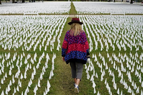 FILE - In this Oct. 27, 2020, file photo, Artist Suzanne Brennan Firstenberg walks among thousands of white flags planted in remembrance of Americans who have died of COVID-19 near Robert F. Kennedy Memorial Stadium in Washington. Firstenberg's temporary art installation, called "In America, How Could This Happen," will include an estimated 240,000 flags when completed. (AP Photo/Patrick Semansky, File)