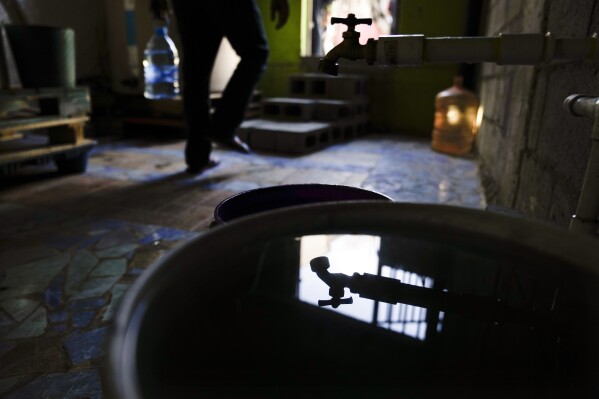 A migrant carries a water jug as he passes a spigot used to fill buckets at the Agape migrant shelter Tuesday, May 9, 2023, in Tijuana, Mexico. Among the last cities downstream to receive water from the shrinking Colorado River, Tijuana is staring down a water crisis. (AP Photo/Gregory Bull)