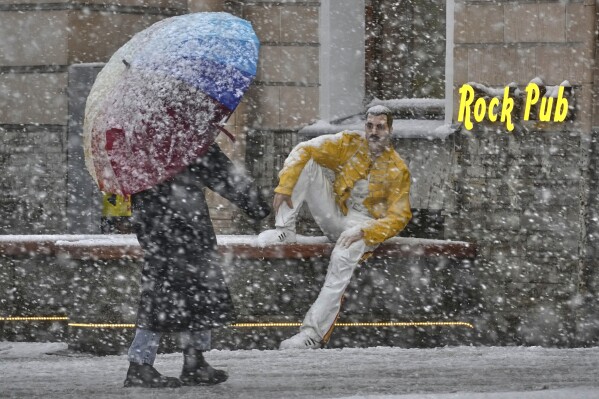 A woman walks past a figure of Queen lead singer Freddie Mercury installed at the entrance of a pub, during a snowfall in St. Petersburg, Russia, Tuesday, March 4, 2025. (AP Photo/Dmitri Lovetsky)
