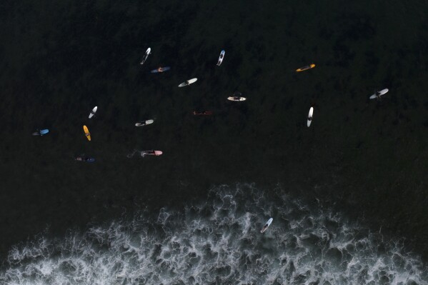FILE - Surfers float in the water while waiting for a wave in Malibu, Calif., Aug. 31, 2023. Earth is exceeding its “safe operating space for humanity” in six of nine key measurements of its health, and two of the remaining three, one being ocean acidity, are headed in the wrong direction, a new study said. (AP Photo/Jae C. Hong, File)