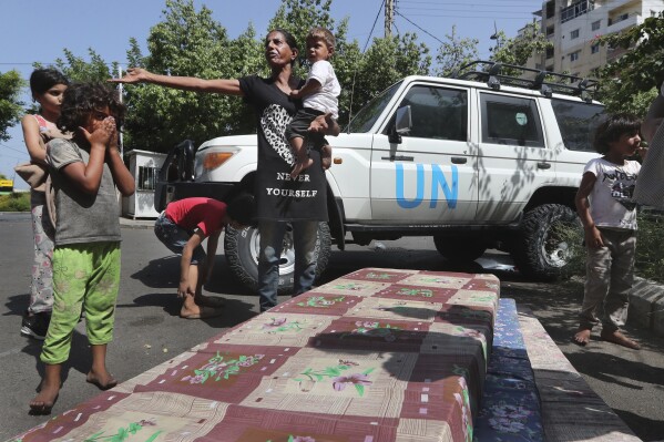 A Palestinian woman stands with her family after fleeing from the Palestinian refugee camp of Ein el-Hilweh, as they wait outside Sidon municipality to be moved to an UNRWA (United Nations Relief and Works Agency for Palestine Refugees in the Near East) school, in the southern port city of Sidon, Lebanon, Tuesday, Sept. 12, 2023. UNRWA said hundreds of families displaced from Ein el-Hilweh refugee camp have taken shelter in nearby mosques, schools and the Sidon municipality building after the fighting that broke out last Thursday in the camp between Palestinian President Mahmoud Abbas' Fatah group and militant Islamist groups which left several people dead and dozens wounded. (AP Photo/Mohammed Zaatari)