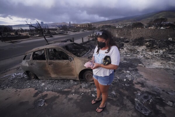 FILE - Summer Gerling picks up her piggy bank found in the rubble of her home following the wildfire on Aug. 10, 2023, in Lahaina, Hawaii. Lahaina residents are grappling with a range of feelings as Maui authorities plan to begin allowing them back into what has become known as the "burn zone." (AP Photo/Rick Bowmer, File)