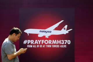 FILE - A man walks past a board reading "Pray for MH370" for passengers aboard a missing Malaysia Airlines plane, in Kuala Lumpur, Malaysia, on March 15, 2014. Malaysia's government on Thursday, June 8, 2023, condemned a Singapore-born stand-up comedian who mocked Malaysia and made fun of the 2014 disappearance of Malaysia Airlines Flight MH370 during a skit in the United States.(AP Photo/Lai Seng Sin, File)