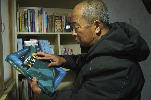 O agricultor chinês Li Eryu olha para um livro escrito sobre o voo MH370 da Malaysia Airlines desaparecido da estante do antigo quarto de seu filho em um vilarejo em Handan, província de Hebei, no norte da China, em 28 de fevereiro de 2024. Li, cujo filho estava no avião, continua para procurar respostas depois de... Década.  O intrigante desaparecimento do voo MH370 continua a cativar pessoas em todo o mundo.  O Boeing 777 partiu de Kuala Lumpur com 239 pessoas a bordo em 8 de março de 2014, mas desapareceu do radar logo depois e nunca chegou ao seu destino, Pequim.  Os investigadores dizem que alguém desligou intencionalmente o sistema de comunicações do avião e tirou o avião do curso.  (Foto AP/Emily Wang Fujiyama)