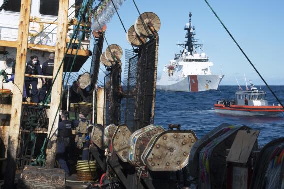 In this photo made available by the U.S. Coast Guard, guardsmen from the cutter James, seen at background right, conduct a boarding of a fishing vessel in the eastern Pacific Ocean, on Aug. 4, 2022. During the 10-day patrol for illegal, unreported or unregulated fishing, three vessels steamed away. Another turned aggressively 90 degrees toward the James, forcing the American vessel to maneuver to avoid being rammed. (Petty Officer 3rd Class Hunter Schnabel/U.S. Coast Guard via AP)