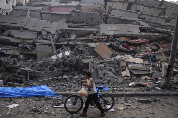 FILE - A Palestinian child walks with a bicycle by the rubble of a building after it was hit by an Israeli airstrike, in Gaza City, Sunday, Oct. 8, 2023. Israel's military offensive has turned much of northern Gaza into an uninhabitable moonscape. When the war ends, any relief will quickly be overshadowed by the dread of displaced families for their future. (AP Photo/Fatima Shbair, File)