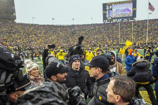 FILE - Ohio State head coach Ryan Day, center left, shakes hands with Michigan head coach Jim Harbaugh, center right, after an NCAA college football game in Ann Arbor, Mich., Saturday, Nov. 27, 2021. The final game of Harbaugh's suspension will be served Saturday, Nov. 25, 2023, keeping the former Michigan quarterback, who finally flipped the rivalry after a decade and a half of dominance by the Buckeyes, off the sideline as his team tries to make it three straight against Ohio State. (AP Photo/Tony Ding, File)