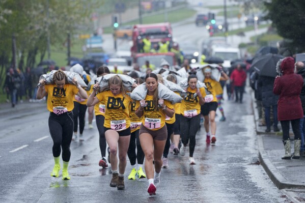 Women's race competitors, including winner Ferne Gardner, front, No. 11, run with a 20kg sack of coal over a 1.1km course during the World Coal Carrying Championships in Ossett, West Yorkshire, England, on Monday, April 21, 2025. (AP Photo/Jon Super)