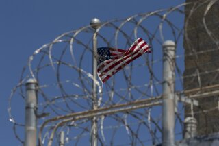 FILE - In this April 17, 2019 file photo reviewed by U.S. military officials, a U.S. flag flies inside the razor wire of the Camp VI detention facility in Guantanamo Bay Naval Base, Cuba. A former CIA contractor who helped design the agency’s harsh interrogation program following the Sept. 11 attacks pushed back Friday on the notion that the survival training for U.S. service members, which became the basis for the “enhanced” techniques used on American captives, amounted to torture.  (AP Photo/Alex Brandon)