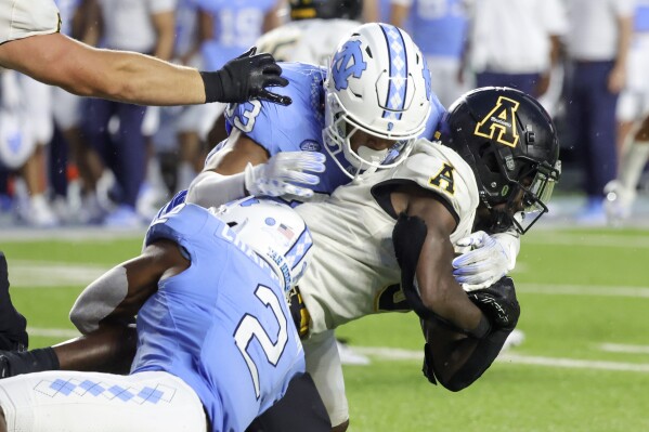 FILE - North Carolina linebacker Cedric Gray (33) and defensive back Don Chapman (2) combine to bring down Appalachian State running back Nate Noel (5) during the second half of an NCAA college football game, Sept. 9, 2023, in Chapel Hill, N.C. North Carolina state legislators advanced a bill Tuesday, June 4, 2024, that would require the state’s two largest public universities — the University of North Carolina at Chapel Hill and N.C. State University — to play each other annually in football and basketball and play three other top public system schools regularly. (AP Photo/Reinhold Matay, File)