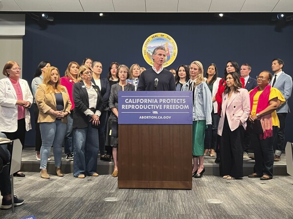 Joined by the state Legislative Women's Caucus and advocates, California Gov. Gavin Newsom, center, speaks during a news conference, Wednesday, April 24, 2024, in Sacramento, Calif., to announce legislation that would help Arizona women access abortions. The proposal would circumvent a ban on nearly all abortions in Arizona by allowing Arizona doctors to give their patients abortions in California. (AP Photo/Sophie Austin)