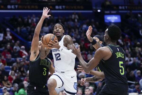 Memphis Grizzlies guard Ja Morant (12) goes to the basket between New Orleans Pelicans guard CJ McCollum (3) and forward Herbert Jones (5) in the first half of an NBA basketball game in New Orleans, Tuesday, Dec. 19, 2023. (AP Photo/Gerald Herbert)