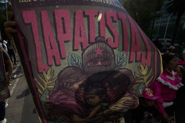 FILE - A supporter of the Zapatista Army of National Liberation, EZLN, holds up a poster whose Zapatista Mayan community was allegedly shot at by paramilitaries, during a march against the recent wave of violence that shook the Mexican state of Chiapas, in Mexico City, Thursday, June 8, 2023. The Zapatista indigenous rebel movement in southern Mexico said in a statement posted Monday, Nov.6, 2023, that it is dissolving the “autonomous municipalities” it declared in the years following the group's 1994 armed uprising. (AP Photo/Fernando Llano, File)