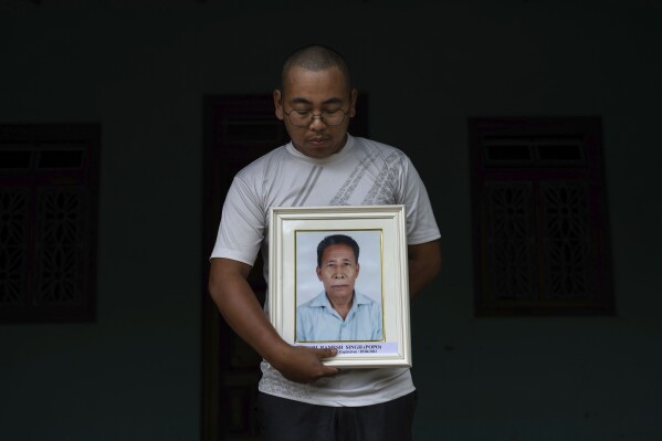 Robert Singh, 26, from the Meitei community, holds a portrait of his father A. Ramesh Singh who was killed by tribal Kukis in Phayeng, near Imphal, capital of the northeastern Indian state of Manipur, Thursday, June 22, 2023. A former soldier, Singh carried a licensed gun with him which he fired in the air and some at the mobs, but was hit in his leg. He was abducted with four others and dragged up the hills and his body found in a grove next day, his son said. He was shot in the head. (AP Photo/Altaf Qadri)