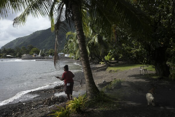 A man burns fallen leaves on a beach in Teahupo'o, Tahiti, French Polynesia, Friday, Jan. 13, 2024. (AP Photo/Daniel Cole)