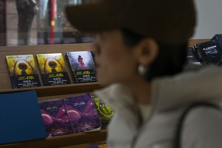 A woman walks past copies of "The Three-Body Problem" on display at a bookstore in Beijing on Monday, Feb. 19, 2024. The series, written by former engineer Liu Cixin, helped Chinese science fiction break through internationally, winning awards and making it onto the reading lists of the likes of former U.S. President Barack Obama and Mark Zuckerberg. (AP Photo/Andy Wong)